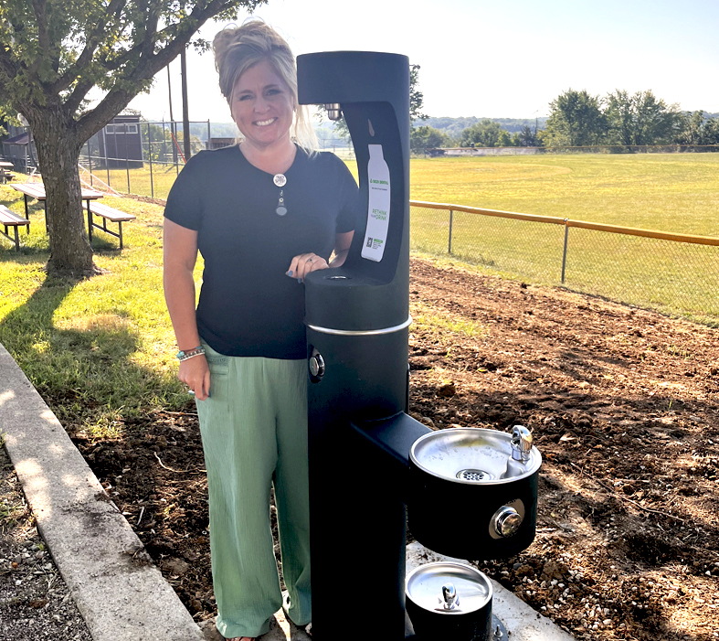 woman smiling while standing next to a new Rethink Your Drink fill station