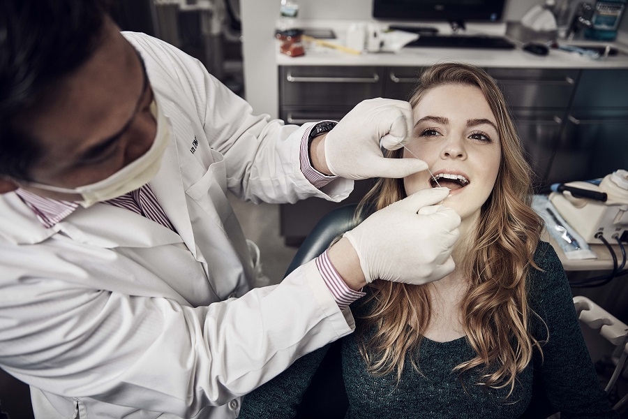 Girl sitting in a dentist chair with the dentist flossing her teeth