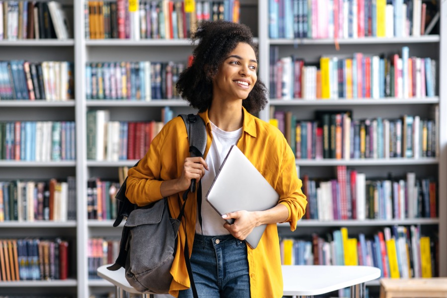 college student in library with backpack and laptop