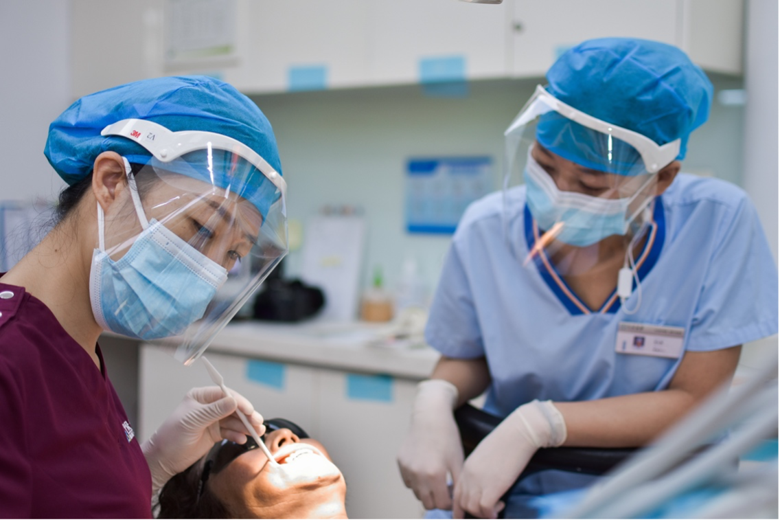 Two dental assistants review a patient’s x-ray on a computer at the dental office desk.