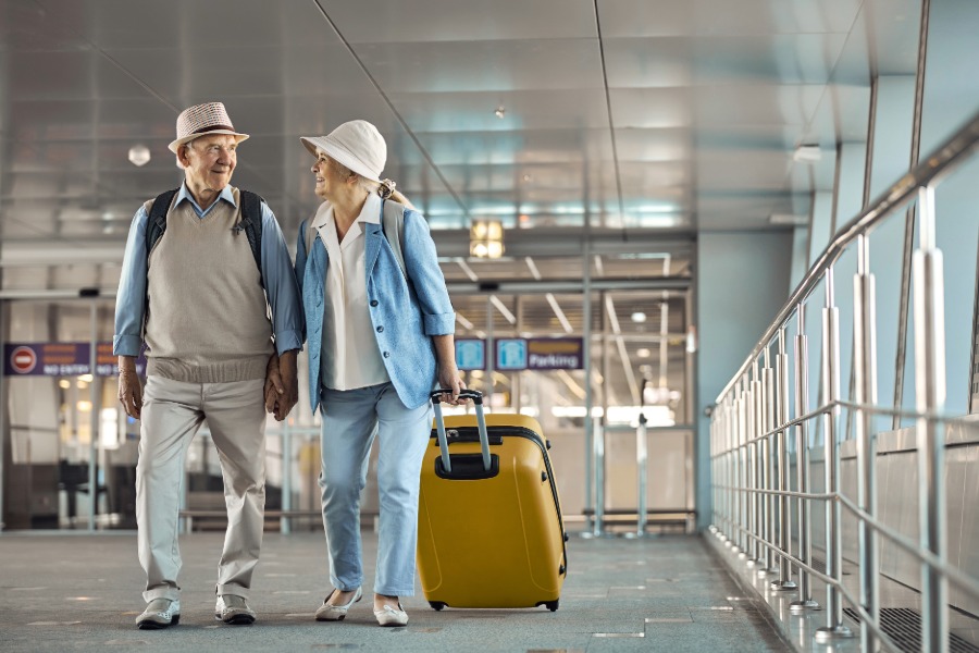 senior man and woman walking in airport with luggage